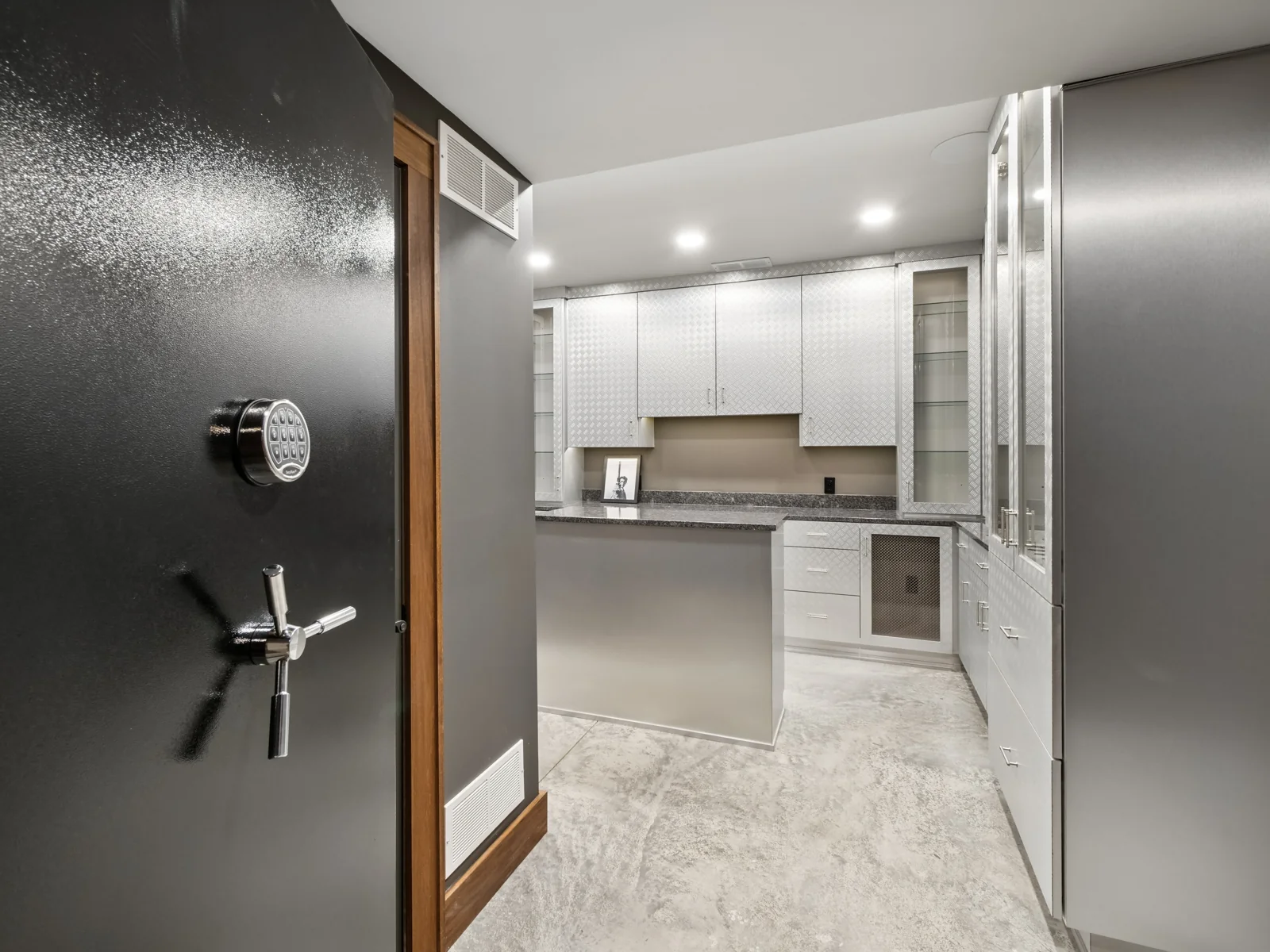 Black vault-style door opening into the private collection room with custom metallic cabinetry and a central island